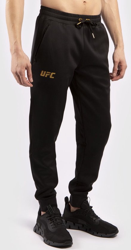 Zwarte trainingsbroek met gouden UFC-logo op de linkerpijp en gouden Venum-logo op de rechterpijp.