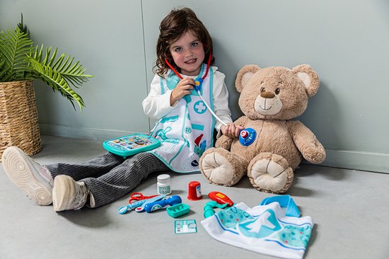 Een jong meisje met een dokterspruim en stethoscoop speelt met een teddybeer.