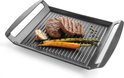 Gegoten aluminium grillplaat met ribbels, waarop twee steaks, een halve knoflook, asperges en wortel liggen. Peperkorrels liggen ernaast.