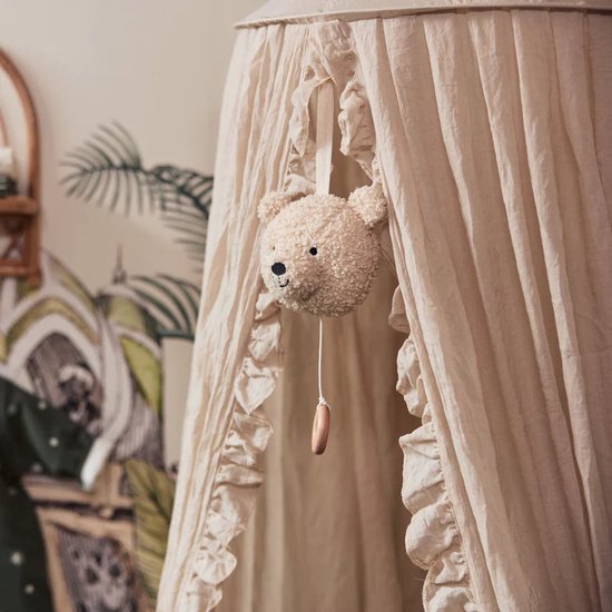 Lichtbruine teddybeer-muziekhanger hangend in een hemelbed.