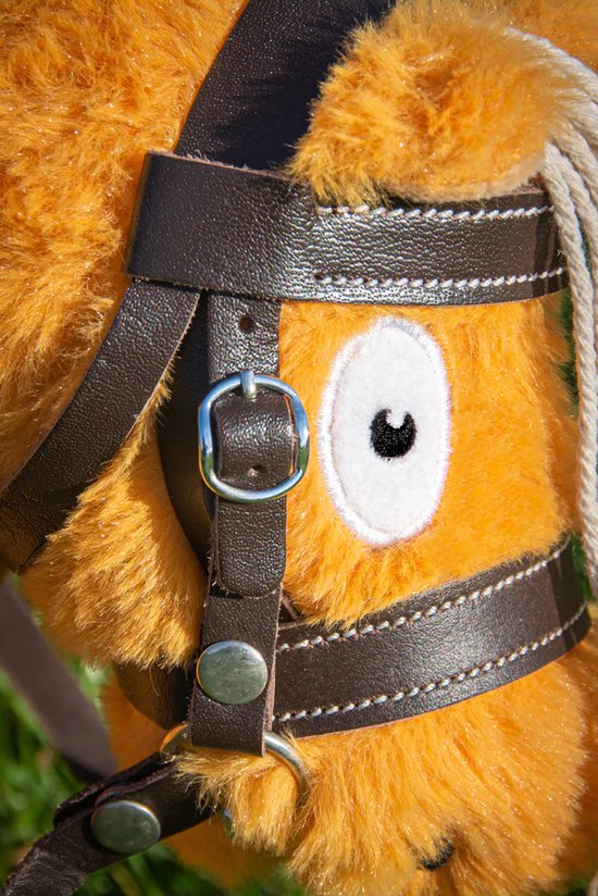 Detail van een oranje knuffelpony met een bruin leren hoofdstel, gesp en witte stiksels.