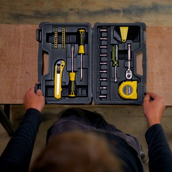 Bovenaanzicht van een zwarte gereedschapskoffer, open op een houten tafel, met gereedschappen in gele en zilveren kleuren.