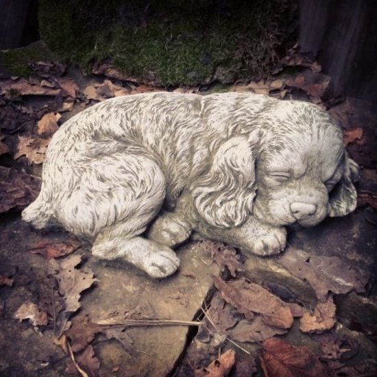 Statue de jardin en béton d'un chiot endormi, avec un pelage détaillé et de longues oreilles.