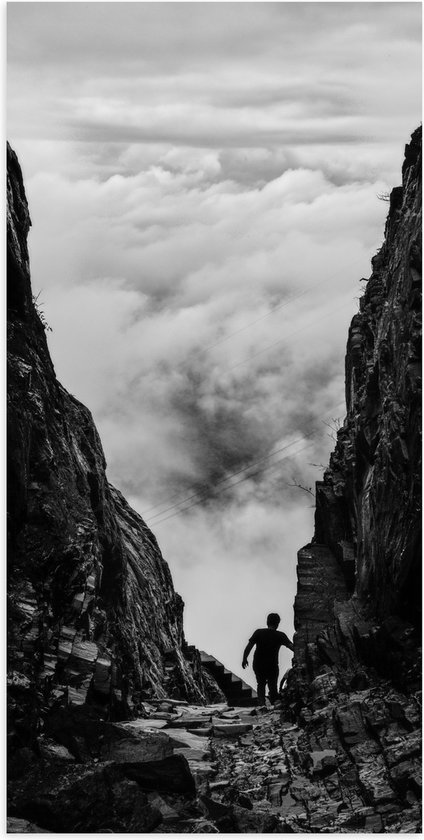 WallClassics - Poster Glanzend – Man tussen Rotsen boven Wolken in Zwart-wit - 50x100 cm Foto op Posterpapier met Glanzende Afwerking