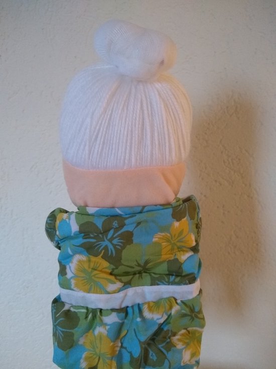 Achterkant van een handpop met wit haar in een knot. Draagt een groen met bloemenprint jurk en wit schort. De mond is gesloten.