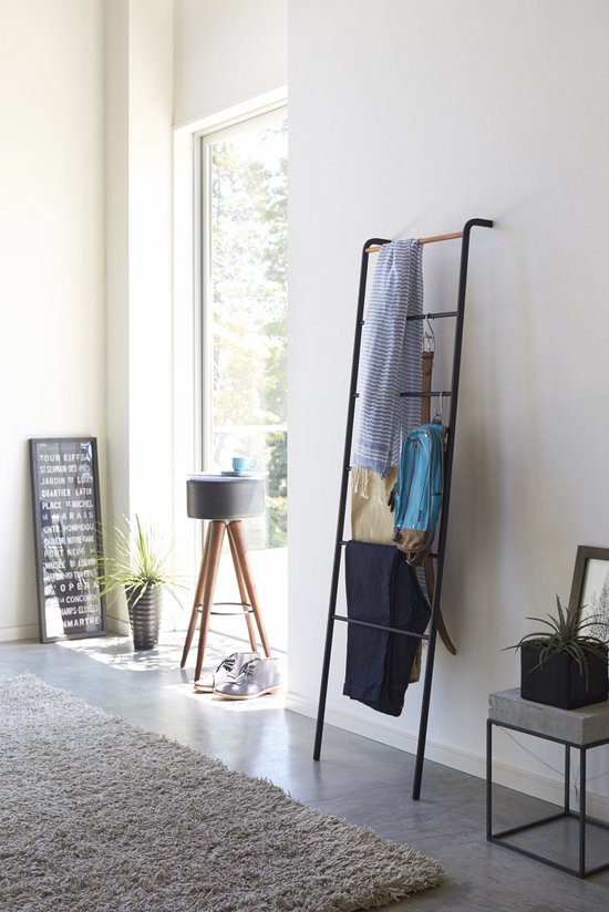 Zwarte ladderrek met kledingstukken: een gestreept textiel, riem, blauwe rugzak, broek en spijkerbroek.