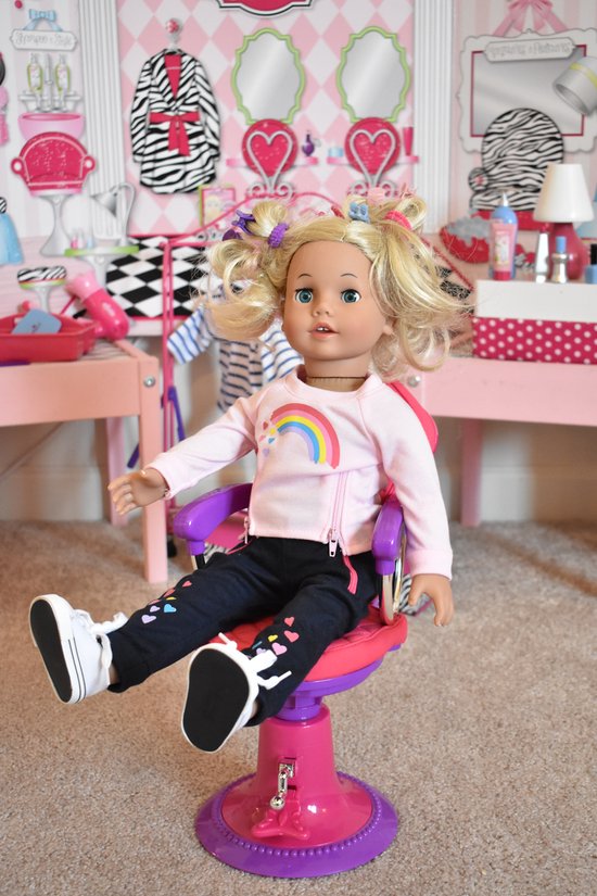 Een pop met blond haar in een roze jack, zittend op een roze kappersstoel.