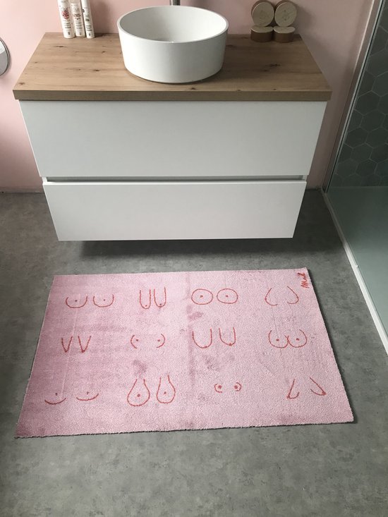 Tapis de bain rose avec un motif de seins orange dans une salle de bain près d'une armoire de lavabo blanche.