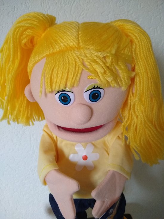 Handpop met blonde staartjes, blauwe ogen, gele trui met witte bloem en spijkerbroek.