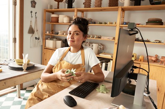 Une femme portant un tablier dans un atelier, avec un clavier HP sur le bureau.