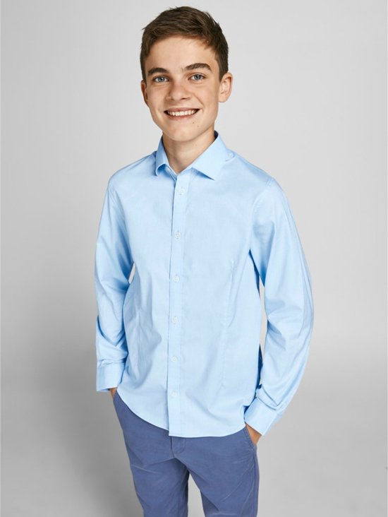 Garçon en chemise blanche bleu clair à manches longues et pantalon bleu, souriant.