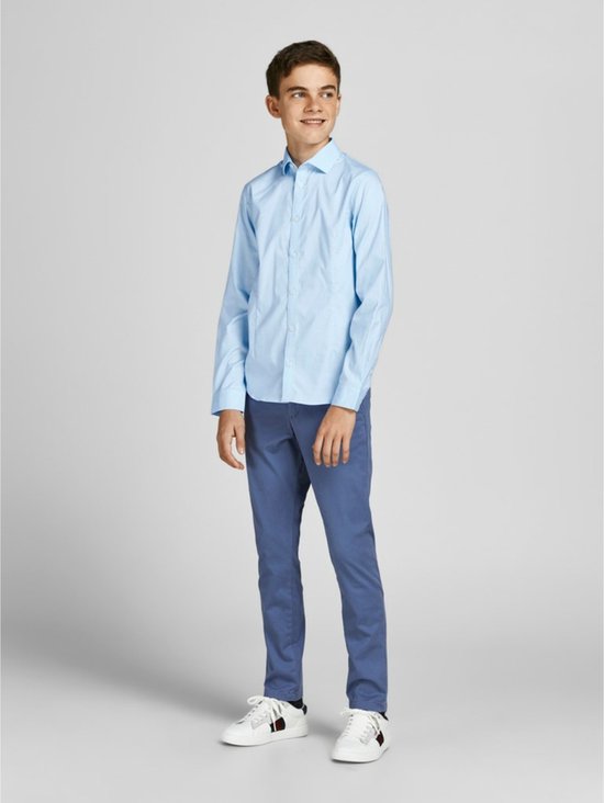 Garçon portant une chemise bleu clair à manches longues et un pantalon habillé, baskets blanches.