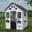 Wit houten speelhuis met zwart dak, zwarte deur, ramen, bloempotten en een groene telefoonhouder.