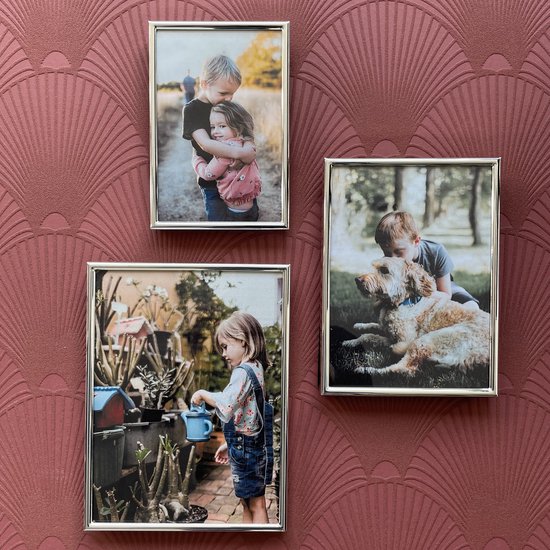 Trois cadres photo argentés présentant des photos d'enfants et d'un chien sur un fond rose.