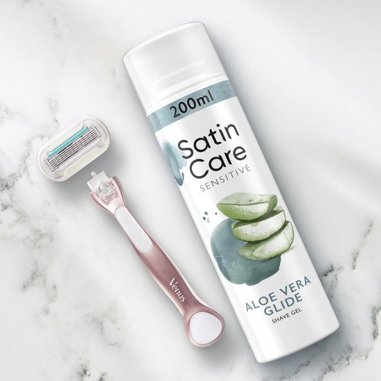 Scheergel bus, scheermesje en een Venus scheermesje liggen op een marmeren achtergrond. Tekst op de bus: '200ml', 'Satin Care SENSITIVE', 'ALOE VERA GLIDE'.