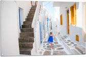 Tuinposter – Meisje in Blauwe Jurk door de Straten van Santorini, Griekenland - 105x70 cm Foto op Tuinposter (wanddecoratie voor buiten en binnen)