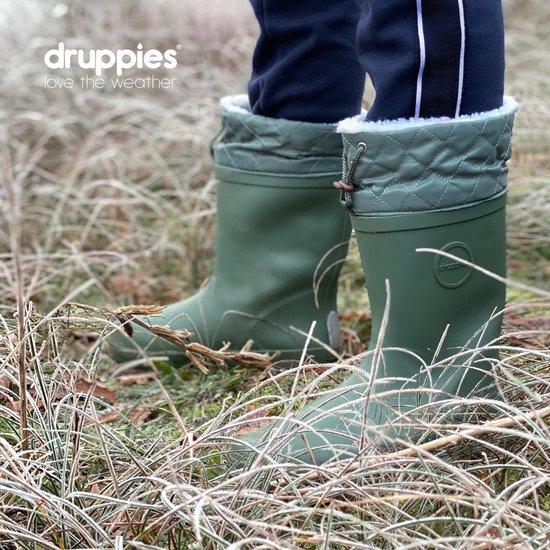Dichtbij van groene winterlaarzen met witte fluffy voering, omringd door droge grasstengels.