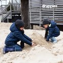 Twee jongens bouwen een zandkasteel op het strand, gekleed in winterkleding en laarzen.
