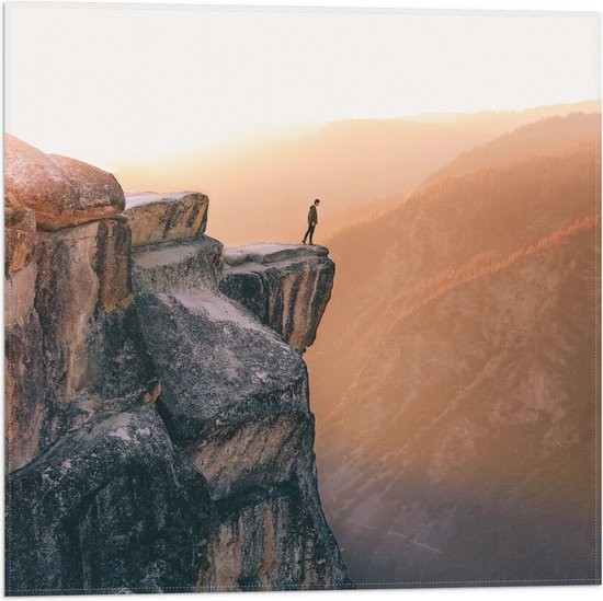 WallClassics - Vlag - Man aan de Rand van Hoge Cliff met Zonlicht - 50x50 cm Foto op Polyester Vlag