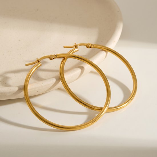 Gouden oorringen van 5 cm, gladde afwerking, op een lichte achtergrond met een gebogen schaal.