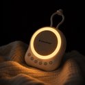 SensaBaby geluidsmachine met zacht licht in een donkere kamer, liggend op een deken. Aura van rust.