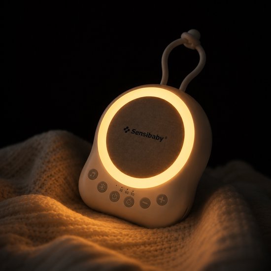 SensaBaby geluidsmachine met zacht licht in een donkere kamer, liggend op een deken. Aura van rust.