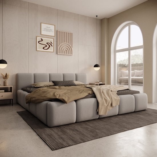 Lit double rembourré gris avec coussins et plaids beiges et marron. Décoration murale beige.