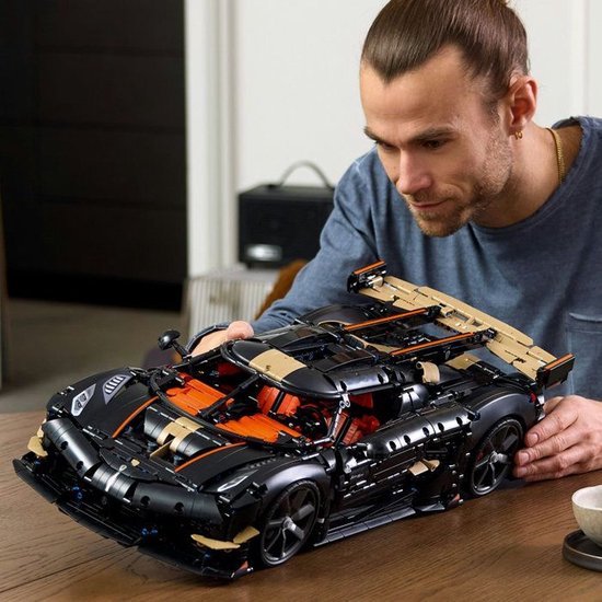 Man bekijkt een gedetailleerde LEGO-auto met zwarte, oranje en gouden kleuren.