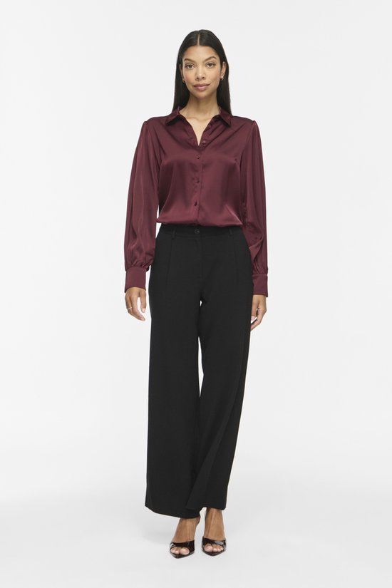 Model in bordeauxrode satijnen blouse met lange pofmouwen en zwarte broek.