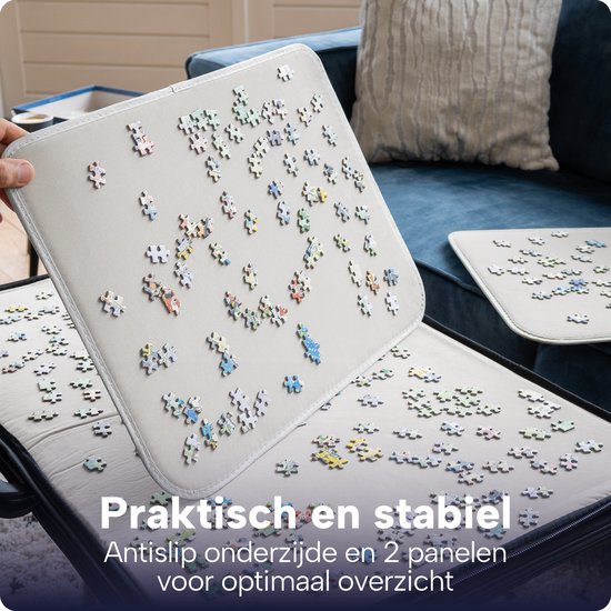 Gedetailleerde foto van een geopende, zwarte puzzelmap met losse puzzelstukjes op de witte panelen. Tekst: Praktisch en stabiel, antislip onderzijde.