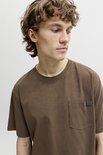 Model met krullend haar in een effen bruin t-shirt met borstzakje en Jack & Jones label.