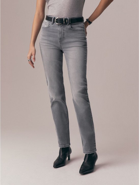 Model in een grijs t-shirt, grijze jeans met zwarte riem en zwarte laarzen.