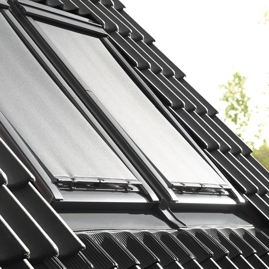 Deux stores pare-soleil noirs pour fenêtres de toit, montés sur un toit en pente avec des tuiles grises.