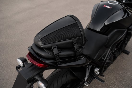 Zwarte motor zadeltas met gaas en gespen, op het zadel van een zwarte motor.