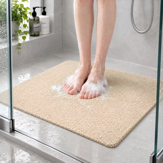 Voeten met schuim op een beige antislip douchemat in een moderne douchecabine.