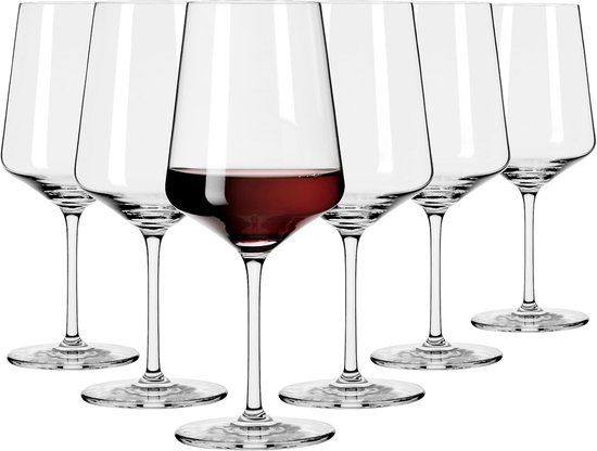 Six verres à vin en cristal, tous sauf un remplis de vin rouge. Hautes tiges et larges calices effilés.