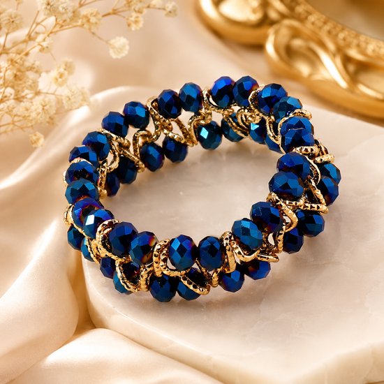 Blauwe facetgeslepen glazen kralenarmband met goudkleurige schakels op een marmeren ondergrond.