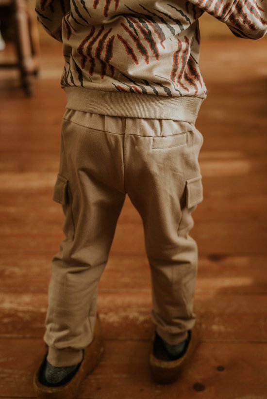 De achterkant van een jongen die een beige joggingbroek met cargo zakken en een trui met tijgerprint draagt.