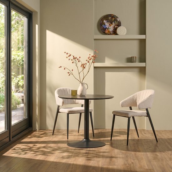 Zwarte ronde tafel met twee crèmekleurige teddy stoelen bij een glazen deur.