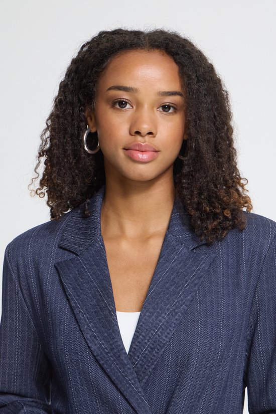 Close-up portret van model met krullend haar in een donkerblauwe krijtstreep blazer.