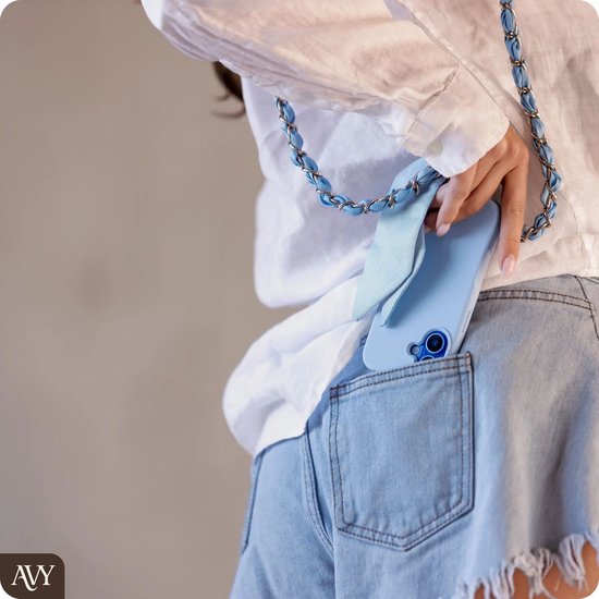 Vrouw in spijkerbroek met witte blouse, stopt lichtblauwe telefoonhoes met ketting in achterzak.