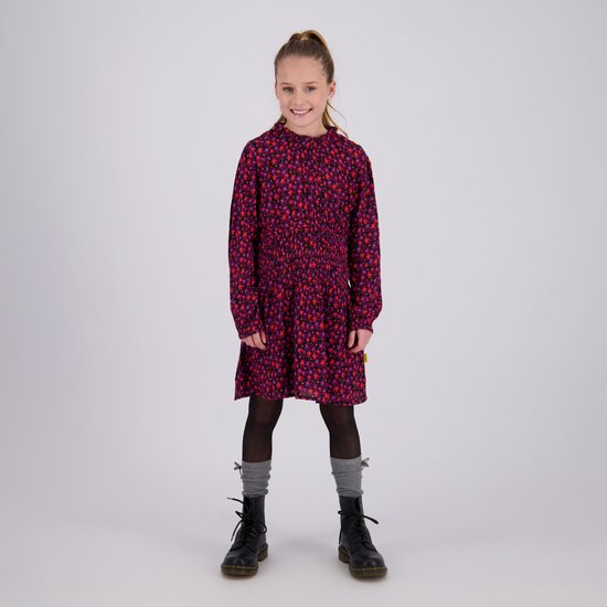 Meisje draagt een rood-paars gebloemde jurk met gesmokte taille, grijze sokken en zwarte veterlaarzen.