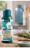 Fles Kneipp Goodbye Stress badolie met watermunt en rozemarijn, op een houten tafel met takjes rozemarijn.