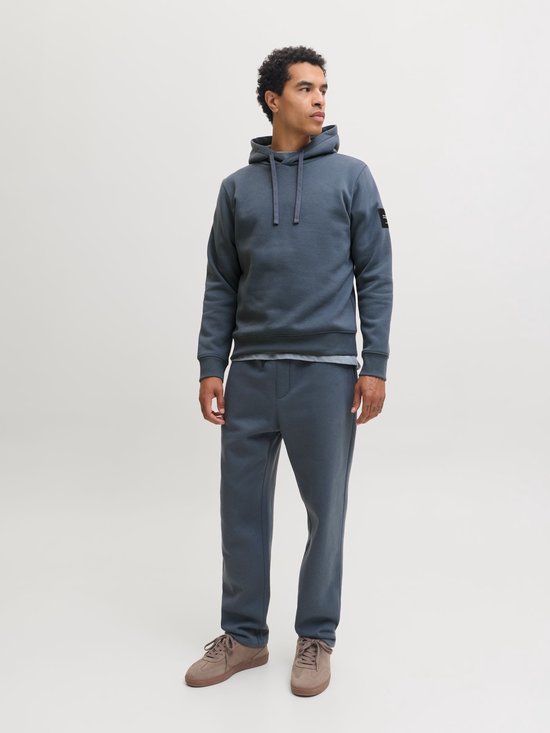 Man in een donkerblauwe joggingbroek met trekkoord en een bijpassende hoodie, sneaker.