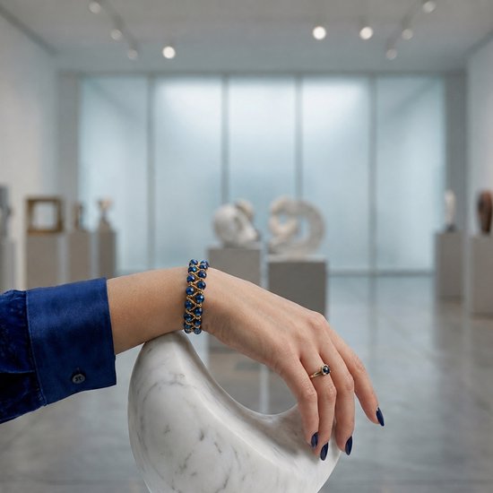 Model draagt een gouden armband met blauwe facetkralen en een bijpassende ring.