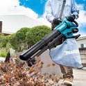 Man in blauw shirt, bruine broek en handschoenen gebruikt een turquoise Makita bladblazer om bladeren te blazen. Blauwe stofzak met 'Makita' tekst.