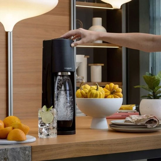 Zwarte SodaStream Terra met bruiswaterfles, glas bruiswater en schijfjes sinaasappel ernaast.