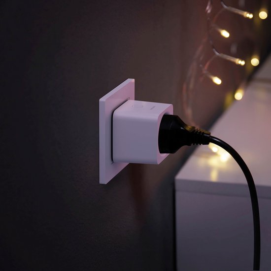 Witte Philips Hue smart plug in een stopcontact, met een zwarte stekker erin, met kerstverlichting.
