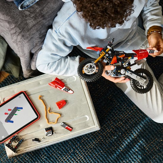 Jongen bouwt aan een LEGO Technic Ducati motorfiets met onderdelen en tablet.