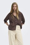 Model draagt een bruine blouse met witte stippen en een off-white wijde broek.